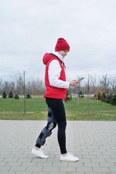 Woman wearing sport clothes and knee brace or orthosis after leg surgery, walking down the stairs in the park. Medical and healthcare concept.