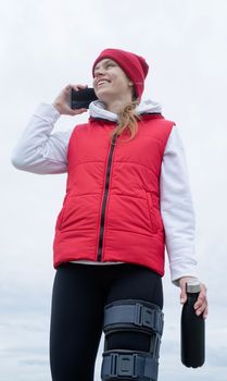 Woman wearing sport clothes and knee brace or orthosis after leg surgery, walking down the stairs in the park. Medical and healthcare concept.