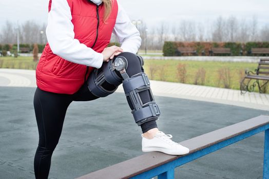 Woman wearing sport clothes and knee brace or orthosis after leg surgery, walking down the stairs in the park. Medical and healthcare concept.