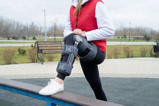 Woman wearing sport clothes and knee brace or orthosis after leg surgery, walking down the stairs in the park. Medical and healthcare concept.