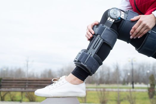 Woman wearing sport clothes and knee brace or orthosis after leg surgery, walking down the stairs in the park. Medical and healthcare concept.