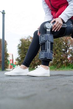 Woman wearing sport clothes and knee brace or orthosis after leg surgery, walking down the stairs in the park. Medical and healthcare concept.