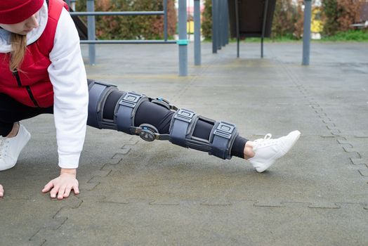 Woman wearing sport clothes and knee brace or orthosis after leg surgery, walking in the park. Medical and healthcare concept.