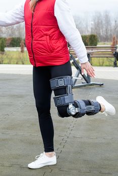 Woman wearing knee brace or orthosis after leg surgery working out in the park . Medical and healthcare concept.