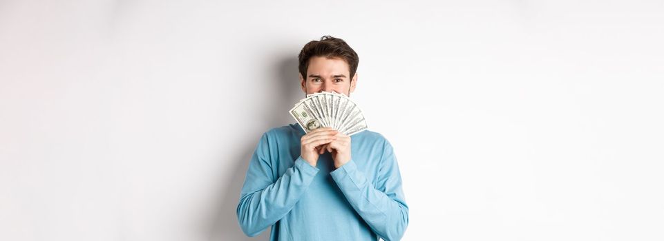 Cheerful shopper holding money for shopping, standing with dollars and smiling, standing over white background in casual clothes.