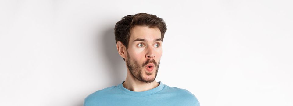 Close-up of impressed caucasian man saying wow, looking left amazed, checking out promotion deal, white background. Copy space