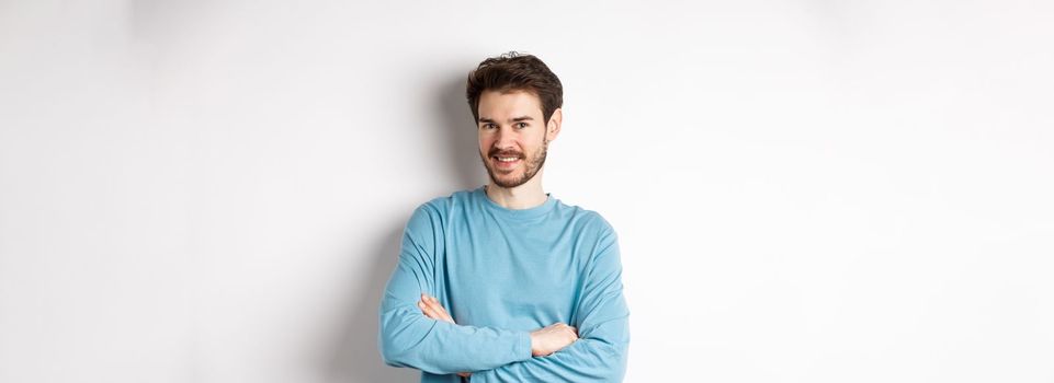 Confident young man with beard, cross arms on chest and smile at camera, standing like professional over white background.