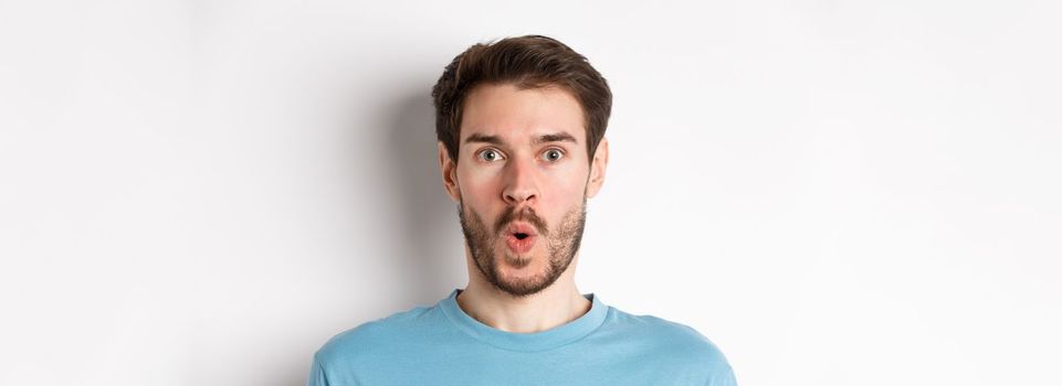 Close-up of surprised man face, saying wow and staring at camera amazed, standing on white background.