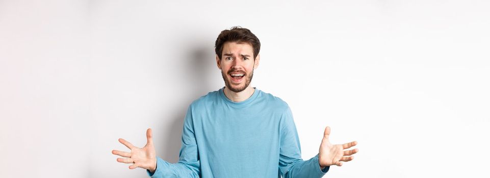 Image of frustrated and worried young man shaking hands, trying to explain something, standing anxious against white background.