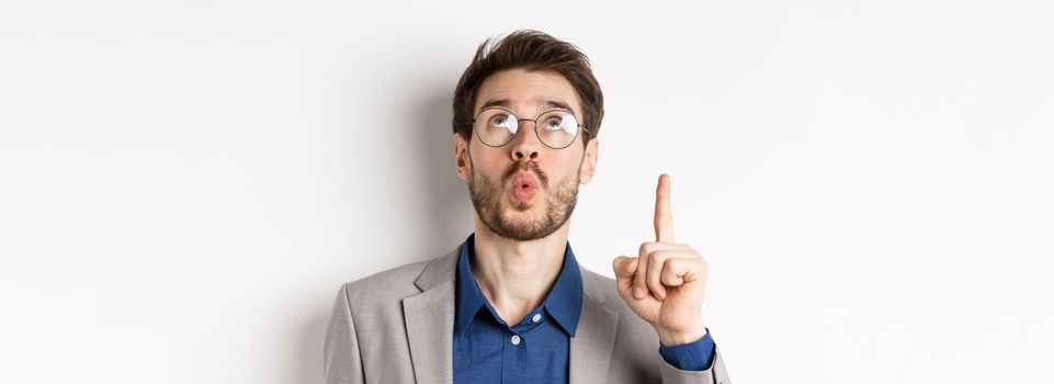 Excited handsome man in glasses and business suit, look up and pointing at top advertisement, exclaim wow with amazed expression, white background.