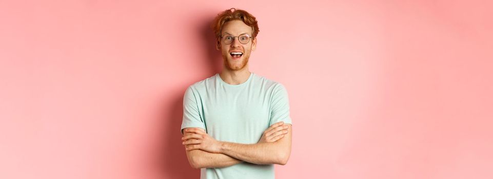 Portrait of cheerful european man in glasses looking amazed at camera, see interesting promotion, standing amused over pink background.