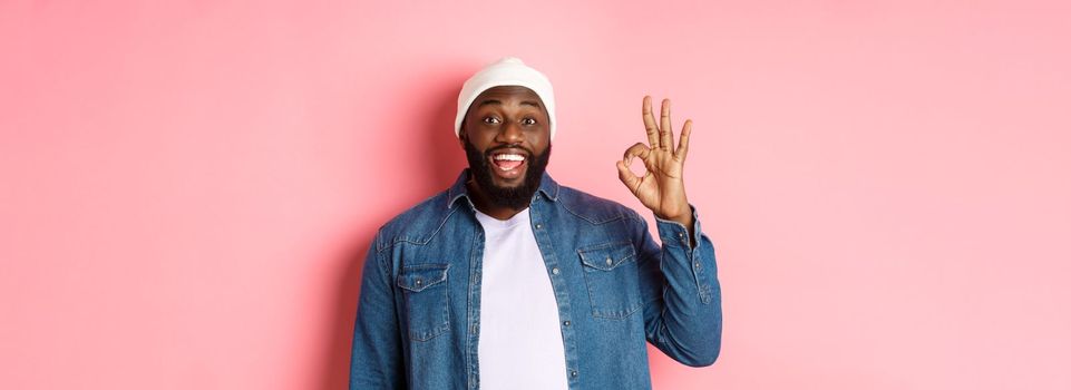 Happy smiling Black guy showing okay sign, approve and praise good offer, standing over pink background.