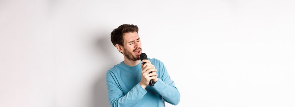 Romantic man singing song in microphone at karaoke, standing over white background.