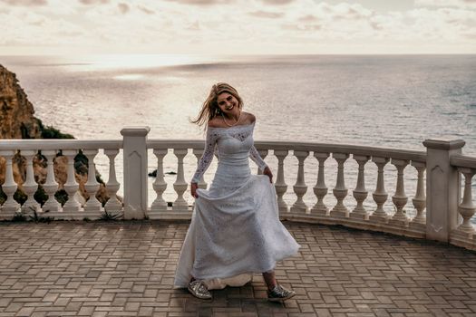 Romantic beautiful bride in white dress posing with sea and mountains in background. Stylish bride standing back on beautiful landscape of sea and mountains on sunset