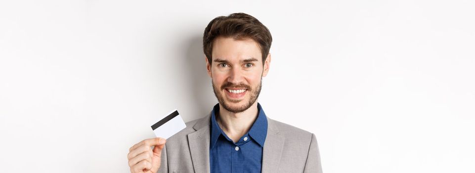 Shopping. Handsome candid business man in suit showing plastic credit card and smiling, recommending bank, white background.