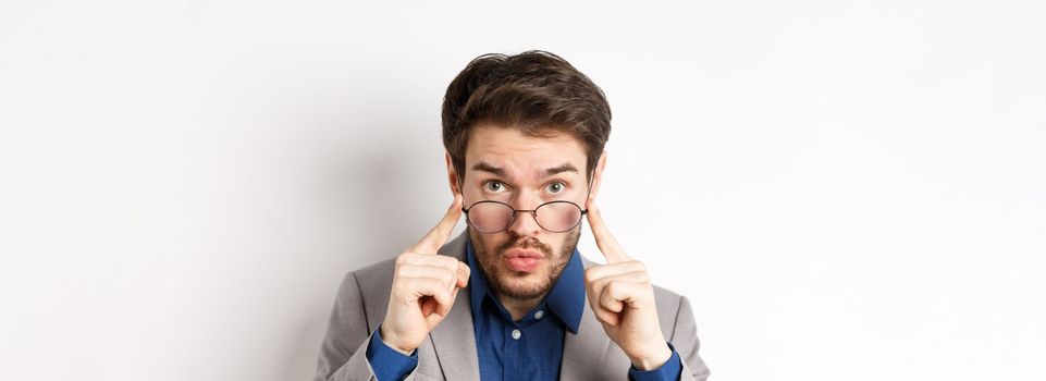 Surprised businessman takes-off glasses and look excited at camera, checking out interesting deal, standing on white background.