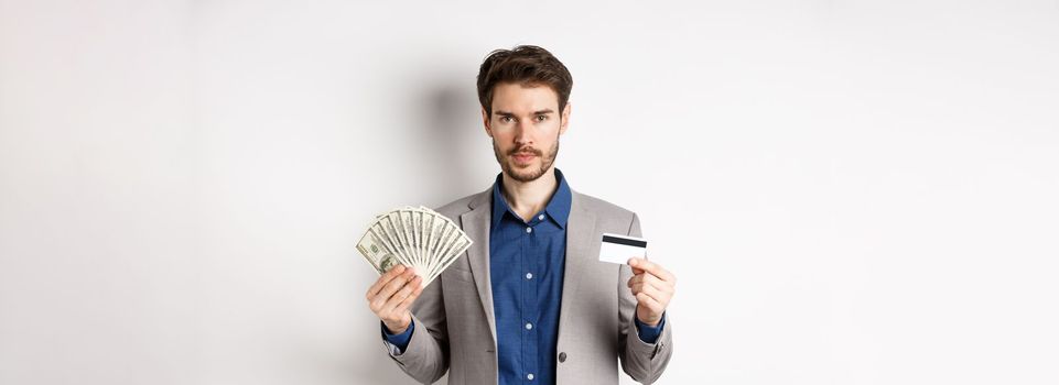 Successful businessman making money, standing in suit with dollar bills and plastic credit card, white background.