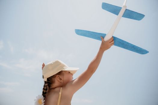 Kid playing with toy airplane. Children dream of travel by plane. Happy child girl has fun in summer vacation by sea and mountains. Outdoors activities at background of blue sky. Lifestyle moment