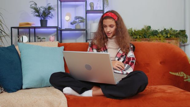 Preteen girl sitting on couch, looking at camera, making video webcam conference call with friends or family, enjoying pleasant conversation. Young teenager child, kid laughing waving hello at home