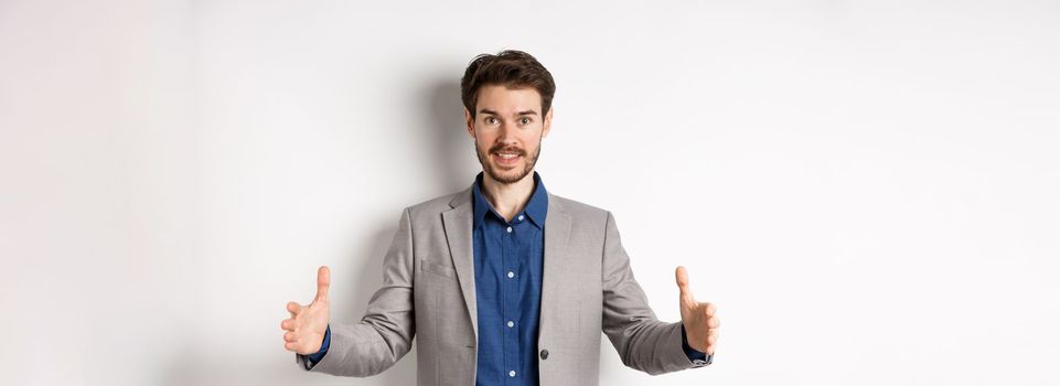 Excited handsome businessman showing long size thing, big object with stretch out hands, standing in suit on white background.