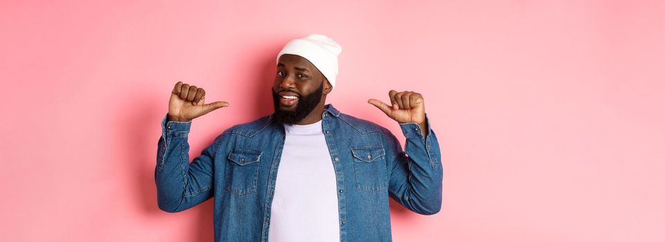 Confident Black bearded man in hipster beanie and denim shirt, pointing at himself with self-assured face, standing over pink background.