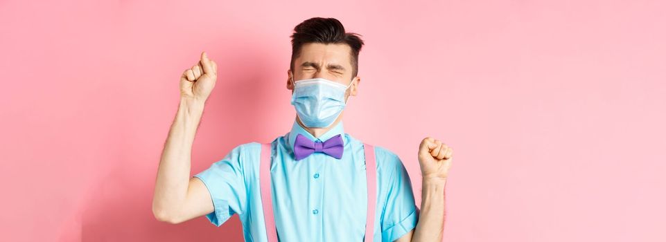 Coronavirus, healthcare and quarantine concept. Frustrated man in medical mask complaining, shaking hands and crying off failure, standing over pink background.