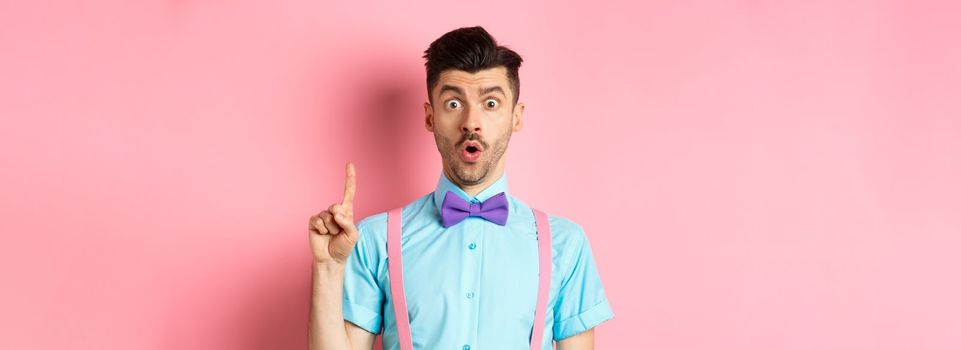 Creative man pitching an idea, saying suggestion with raised finger, standing on pink background.