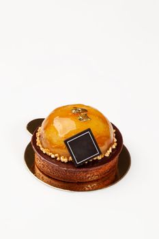 Delicious shortbread tartlet with almond cream, passion fruit caramel and caramelized apples decorated with chocolate, edible gold flakes and nut crumbs on white background
