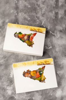 Two carton boxes with colorful marzipan fruits, traditional Sicilian sweets in shape of real fruits made of almond paste on gray background. Example of creativity and mastery of pastry art
