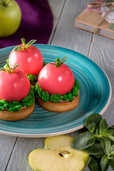 Delicate apple shaped mousse dessert covered with glossy pink glaze on shortcrust tartlets with walnuts layer and green moss of sponge cake served on plate. Natural treats for sweet tooth