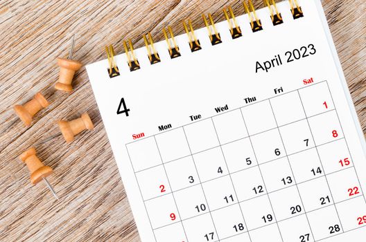 April 2023 Monthly desk calendar for 2023 year with pin on wooden background.