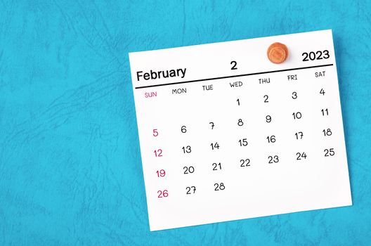 February 2023 monthly calendar and wooden push pin on blue background.