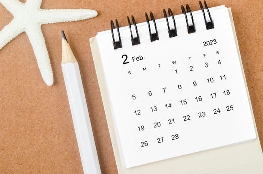 February 2023 Monthly calendar with Starfish and pencil on wooden background.
