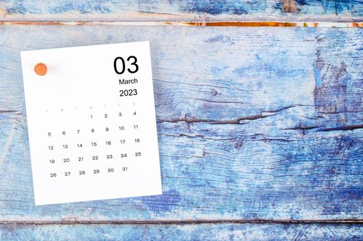 March 2023 monthly calendar and wooden push pin on blue wooden background.