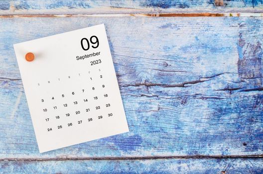 September 2023 monthly calendar and wooden push pin on blue wooden background.