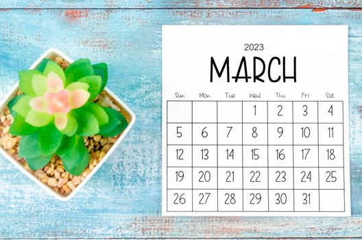 March 2023 Monthly calendar with plant pot on wooden background.