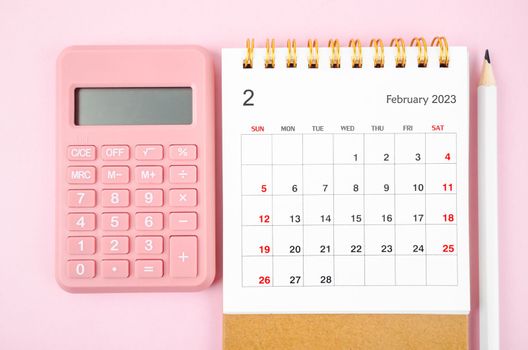 February 2023 desk calendar for 2023 year with calculator on pink color background.
