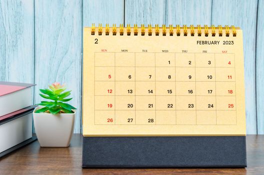 February 2023 Monthly desk calendar for 2023 year with the books on blue wooden background.
