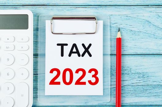 Tax 2023 text on clipboard with calculator on wooden background. 2023 taxation concept.
