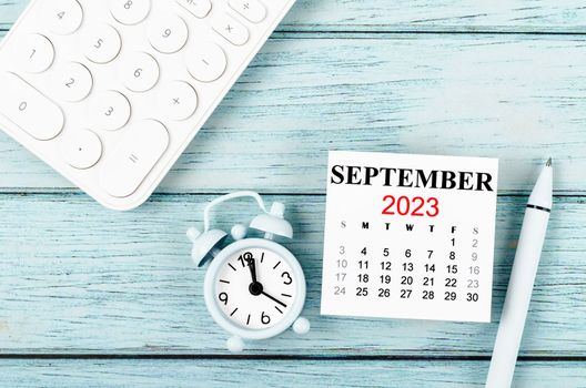 September 2023 Monthly calendar year and alarm clock with calculator on blue wooden background.