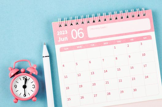 June 2023 desk calendar for 2023 year with alarm clock and pen on blue background.