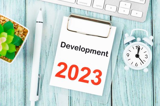 Development 2023 text on clipboard with pen and keyboard computer on wooden background.
