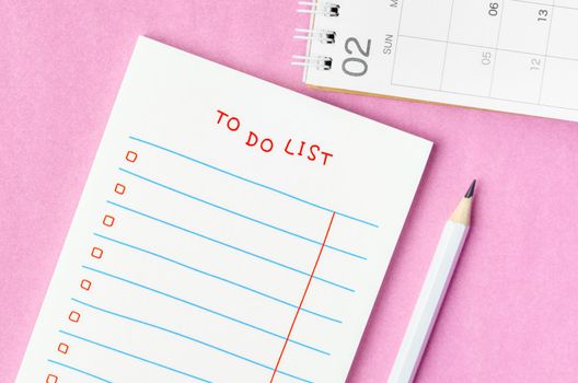 Blank To do list in notepad and desk calendar with wooden pencil on pink background. Top view