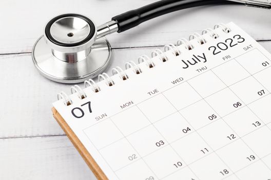 Stethoscope medical and July 2023 desk calendar on wooden background, schedule to check up healthy concepts.