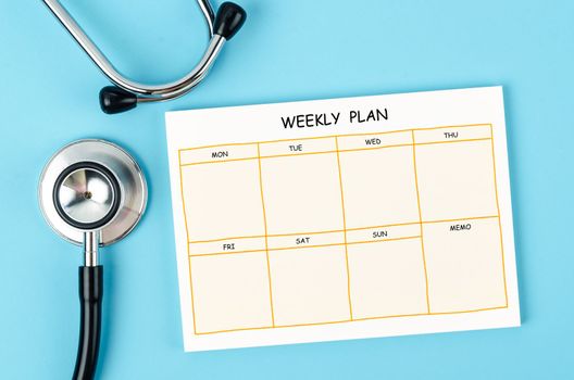Blank weekly plan notice block and medical stethoscope on blue colour background.