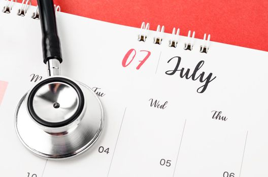 Stethoscope medical and July 2023 desk calendar on the red background, schedule to check up healthy concepts.