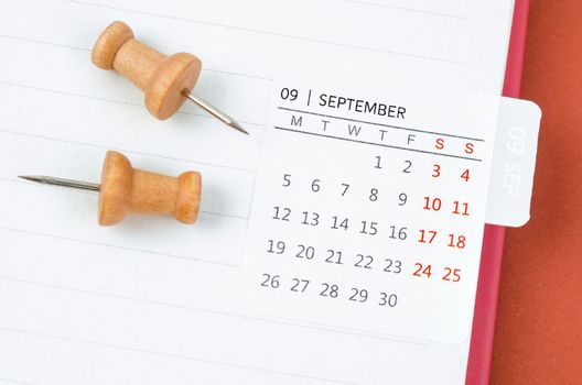 Mini September monthly calendar and wooden push pin on open diary.