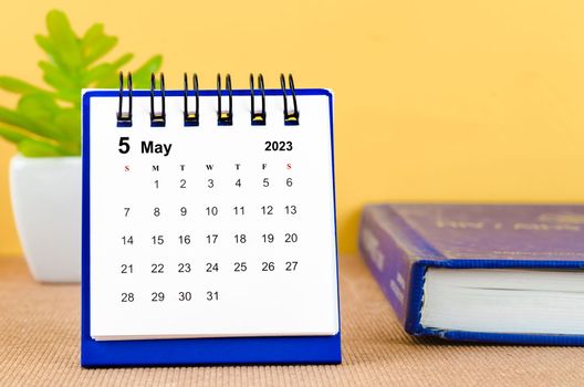 May 2023 Monthly desk calendar for 2023 with a book on yellow background.