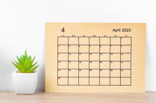 Brown April 2023 Monthly calendar for 2023 year with plant pot on wooden table.
