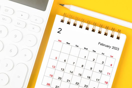 February 2023 Monthly desk calendar for 2023 year and calculator with pen on yellow background.